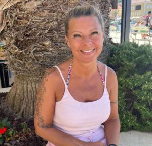 Claudia Hess lächelt in die Kamera, sitzt vor einem Baum im Freien