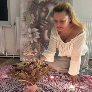 Claudia Hess mit einem getrockneten Blumenstrauss, hinter ihr ein gemaltes Bild eines Frauengesichts