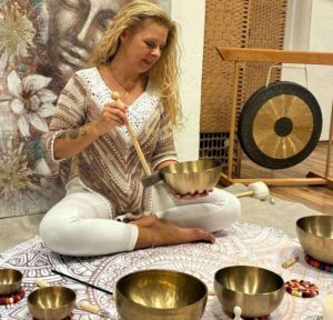 Claudia Hess sitzt auf dem Boden umgeben von Klangschalen in verschiedenen Größen