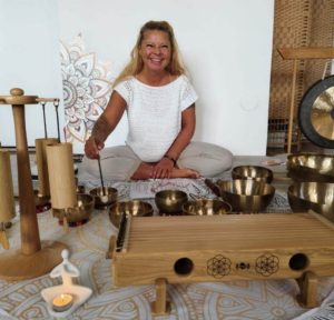 Claudia Hess mit diversen Klangschalen und Klangobjekten sitzt auf dem Boden