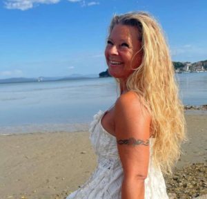 Claudia Hess sitzt am Strand und lächelt in die Kamera